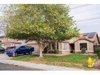 Inviting single-story home with a well-maintained lawn, mature tree, and solar panels on the roof at 1514 E Hearne Way, Gilbert, AZ 85234