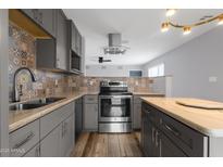 Well-lit kitchen with stainless steel appliances, gray cabinetry, beautiful backsplash, and a kitchen island at 1210 E Harmony Cir, Mesa, AZ 85204