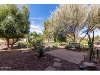 Beautiful backyard featuring desert landscaping, a stone patio, mature trees and a bench at 42906 W Darter Dr, Maricopa, AZ 85138