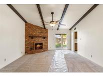 Spacious living room featuring a brick fireplace, exposed beam ceiling, and access to the backyard at 4312 W Paradise Dr, Glendale, AZ 85304