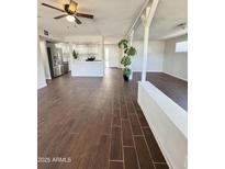 Spacious living room featuring wood-look tile floors, bright lighting, and an open-concept layout to the kitchen at 5729 N 64Th Dr, Glendale, AZ 85301