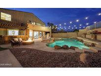 Inviting backyard featuring a pool with waterfall, spa, fire pit, and an outdoor kitchen perfect for evening entertaining at 9867 S 182Nd Dr, Goodyear, AZ 85338