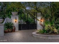 Elegant gated entrance featuring a paver driveway, lush landscaping, and stone pillars with antique sconces, exuding privacy and sophistication at 4900 E Desert Fairways Dr, Paradise Valley, AZ 85253