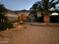 Inviting front yard featuring a desert landscape, palm tree, stone walkway, and warm lighting accents at 16019 W Heritage Dr, Sun City West, AZ 85375