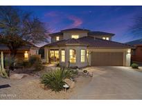 Stunning two-story home featuring desert landscaping, a tile roof, and a two-car garage, all beautifully illuminated at twilight at 11617 E Raintree Dr, Scottsdale, AZ 85255