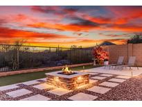 An outdoor living space with a stone fire pit, paver patio, desert view, and lush landscaping at sunset at 30816 N 138Th Ave, Peoria, AZ 85383