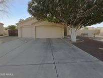 Beige single-story home featuring a dual garage and mature landscaping with a tree at 3313 N Lakeshore Ct, Avondale, AZ 85392