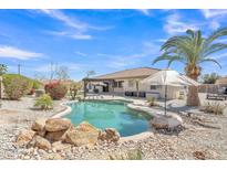 Backyard pool featuring a rock waterfall, pergola, and lush landscaping under a clear blue sky at 14612 W Edgemont Ave, Goodyear, AZ 85395