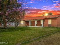 Charming brick home with covered porch, lush lawn, and beautiful sunset backdrop at 1736 E Coronado Rd, Phoenix, AZ 85006