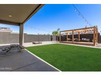 Expansive backyard featuring a wooden pergola, lush grass, gravel accents, and a cozy fire pit, perfect for outdoor entertaining at 1781 S 223Rd Dr, Buckeye, AZ 85326