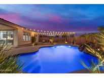 Relaxing backyard oasis with a sparkling pool, stone waterfall feature, desert landscaping, and festive string lights at 10455 E Thornton Ave, Mesa, AZ 85212