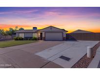 Charming single-story home featuring a spacious driveway, a two-car garage, and a manicured front lawn at sunset at 1840 N Brighton Cir, Mesa, AZ 85207