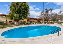 Outdoor pool with lounge chairs and grassy area in front of building on a bright sunny day at 355 E Thomas Rd # B110, Phoenix, AZ 85012