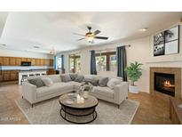 Inviting living room featuring a fireplace, ceiling fan, and a smooth transition to the kitchen area at 3410 E Pageant Pl, Gilbert, AZ 85297