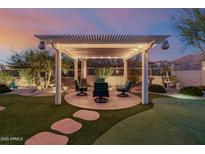 Cozy backyard with a covered patio, outdoor seating and putting green at twilight at 7952 E Teton Cir, Mesa, AZ 85207