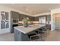 Contemporary kitchen featuring stainless steel appliances, a marble countertop island with seating, and sleek gray cabinetry at 24066 S 218Th Pl, Queen Creek, AZ 85142