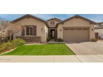 Inviting single-story home with manicured lawn, brick driveway, and a charming stone-accented facade at 20325 E Hummingbird Dr, Queen Creek, AZ 85142
