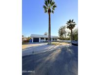 Charming home featuring a large palm tree, manicured lawn, and a driveway leading to an attached garage at 1837 W Virginia Ave, Phoenix, AZ 85007