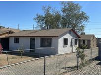 A charming single-story home features a white exterior, chain-link fence and mature trees against a clear blue sky at 2837 W Almeria Rd, Phoenix, AZ 85009