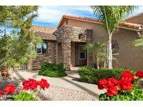 Charming single-story home featuring stacked stone accents and a well-manicured front yard with colorful flowers and palm trees at 2165 Leisure World --, Mesa, AZ 85206