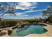 Backyard pool area featuring rock waterfall and desert landscaping with expansive views of the surrounding mountains at 42211 N Long Cove Way, Anthem, AZ 85086