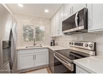 Modern kitchen with stainless steel appliances, white cabinets, tile backsplash, and a bright window at 19400 N Westbrook Pkwy # 241, Peoria, AZ 85382