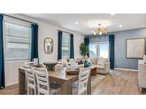 Elegant living room with hardwood floors, modern chandelier, and large windows with blue curtains at 23997 W Cocopah St, Buckeye, AZ 85326