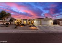 Elegant home exterior at dusk featuring a three-car garage, desert landscaping, and a colorful sky at 3125 W Desert Ln, Laveen, AZ 85339