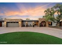 Inviting single-story home featuring a stone facade, arched entryway, and circular driveway with green lawn at 3348 E Eva St, Phoenix, AZ 85028