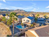 This aerial view showcases a beautiful home with a backyard pool, palm trees, and mountain views at 22491 W Woodlands Ave, Buckeye, AZ 85326