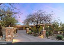 Long driveway leading up to a sprawling home with stone accents and mature trees at dusk at 11988 E Larkspur Dr, Scottsdale, AZ 85259