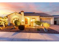 Inviting single-story home with a well-manicured front yard, warm lighting, and a charming entryway, at dusk at 18322 W Thistle Landing Dr, Goodyear, AZ 85338