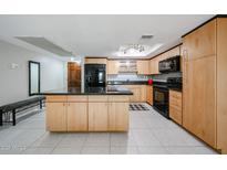 Bright kitchen with stainless steel appliances, tile floors, light wood cabinets, and a black island at 7860 E Camelback Rd # 309, Scottsdale, AZ 85251