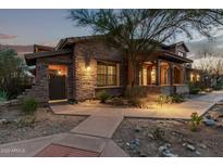 Charming stone home featuring a covered porch with wooden beams and professionally landscaped front yard at dusk at 17902 N 93Rd Way, Scottsdale, AZ 85255