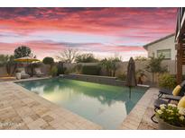 Inviting pool featuring a tanning ledge, mature landscaping, and an open patio with lounge chairs under a colorful sky at 20594 S 194Th Pl, Queen Creek, AZ 85142