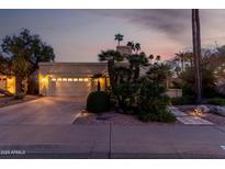 Inviting single-Gathering home featuring a two-car garage, tropical landscaping, and warm exterior lighting at twilight at 8737 E San Vicente Dr, Scottsdale, AZ 85258