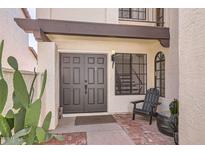 Inviting front entrance with a brown double door, a chair and a cactus at a white, two-story home at 11011 N 92Nd St # 1019, Scottsdale, AZ 85260