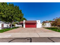 Charming home featuring a red garage door, brick driveway, green landscaping, and a white exterior at 5324 W Carol Ave, Glendale, AZ 85302