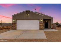 Charming home exterior featuring a large garage, stylish stone accents, and desert landscape at 21816 W Taft Ave, Wittmann, AZ 85361