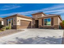 Tan single-Gathering home with a large driveway and desert landscaping with a two car garage and stone accents at 25983 W Escuda Dr, Buckeye, AZ 85396