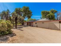 Charming single-story home featuring mature trees and a spacious dirt driveway, set under a bright blue sky at 6648 S 27Th Ave, Phoenix, AZ 85041