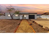 Inviting single-story home with desert landscaping, complemented by a black garage door, and arched entryway at sunset at 18060 N 24Th Dr, Phoenix, AZ 85023