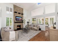 Bright living room featuring a stone fireplace, large windows with shutters, and hardwood floors at 4151 E Mercer Ln, Phoenix, AZ 85028