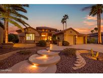 Elegant home featuring lit entryway steps, a stone facade, and lush desert landscaping at twilight at 15751 W Linksview Dr, Surprise, AZ 85374