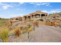 Grand Southwestern-style home features desert landscaping, a circular design, and a paved driveway leading to the gated entrance at 14360 E Desert Cove Ave, Scottsdale, AZ 85259