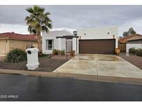 Contemporary home with white stucco, a brown garage door, gated front entrance, and desert landscaping at 10406 E Silvertree Dr, Sun Lakes, AZ 85248