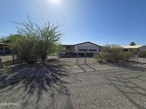 Modest single-story home featuring a secure fenced yard, mature trees, and gravel landscaping at 10997 N Hualapai Dr, Casa Grande, AZ 85122