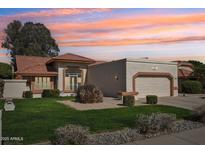 Charming single-story home with a tile roof, well-maintained lawn and desert landscaping at sunset at 13942 W Summerstar Dr, Sun City West, AZ 85375