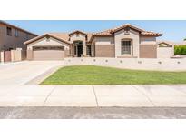 Tan home featuring an arched front door, 2-car garage, decorative wall, and lush green lawn at 6920 W Tether Trl, Peoria, AZ 85383