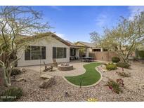 A cozy backyard featuring a stone fire pit, seating, artificial turf, desert landscaping, and mature trees at 2544 W Pumpkin Ridge Dr, Anthem, AZ 85086